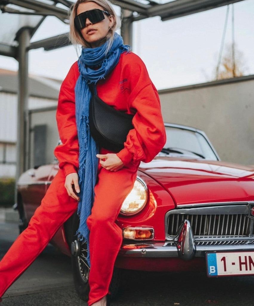 Photo d'une femme habillée en rouge avec une écharpe saint gervais bleu, assise sur une voiture rouge décapotable. 